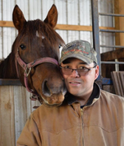 On the left is a horse nuzzling up to Paul Simon, wearing work close and hat, on the right.